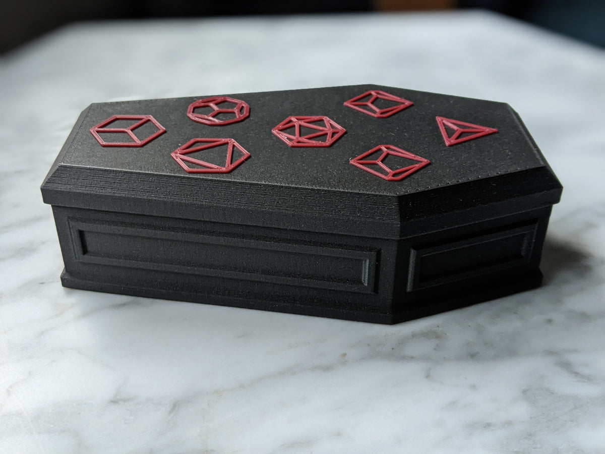 Closed black coffin dice vault with red polyhedral dice outlines on the lid